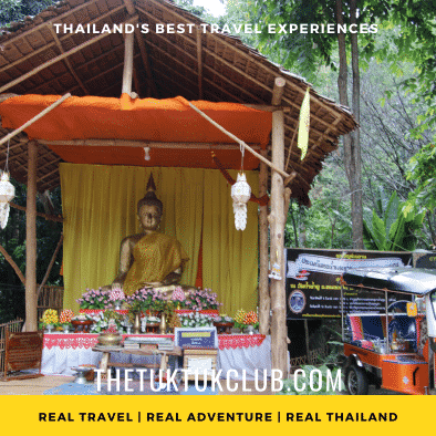 A small wooden hut with a golden Buddha and offerings inside in a forest in Chiang Mai