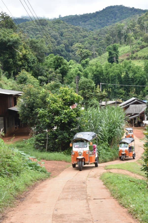 A convoy of three Tuk Tuks driving up a small track in a mountain Hill Tribe village in Northern Thailand
