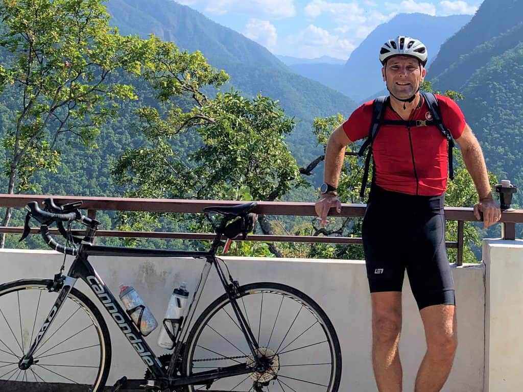 A cyclist standing next to a bike with the high mountains of Mae Hong Son in the background